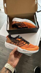 "New Balance Fuel Cell Venym in hand showcasing its vibrant orange and black design."