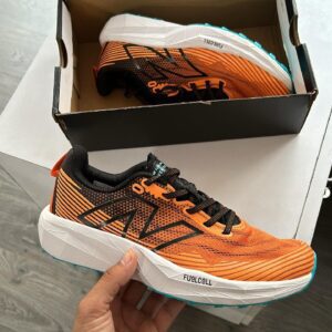 "New Balance Fuel Cell Venym in hand showcasing its vibrant orange and black design."